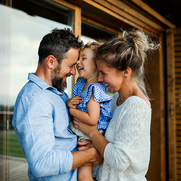 man and woman holding a toddler between them, standing on a porch