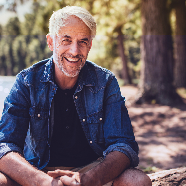 Senior man sitting by a lake, smiling at camera